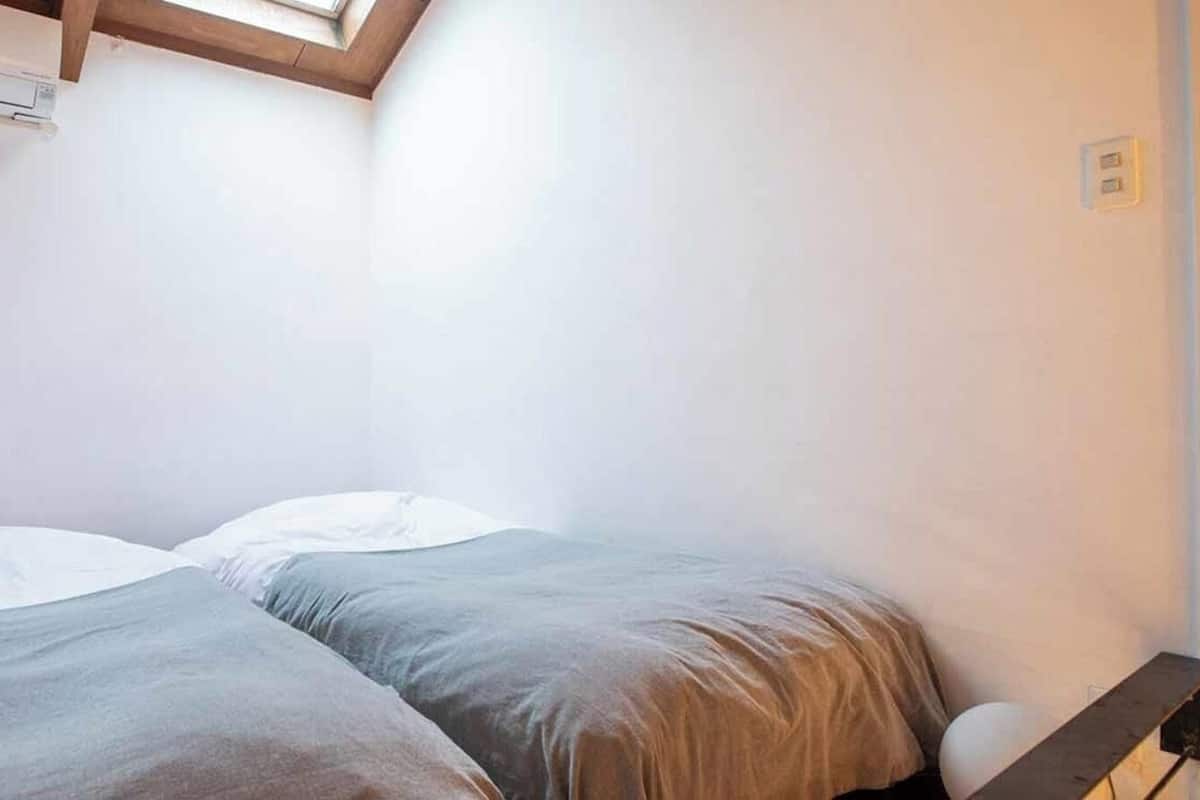 Una habitación pequeña con una cama individual, techo inclinado, cabecera de madera y aire acondicionado de pared.