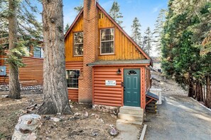 A rustic log cabin with a green door, a small porch, and a stone wall foundation. - Silvertip Pines #2335 (Big Bear Lake)