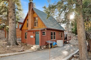 A log cabin with a chimney, a porch, and a small table with items on it. - Silvertip Pines #2335 (Big Bear Lake)
