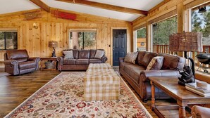 A wooden interior with a sofa set, a patterned rug, and a dining table.
