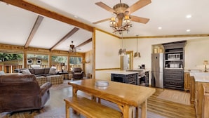 A spacious living area with a wooden dining table, sofas, and a ceiling fan.
