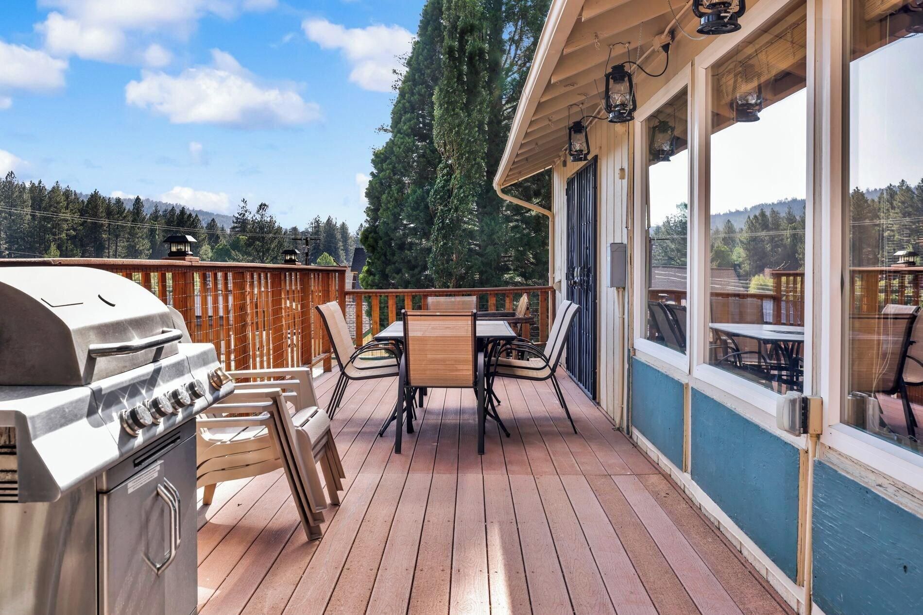 A deck with a grill, chairs, and tables, overlooking a forested area.