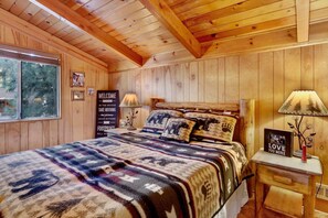 A wooden cabin room with a bed, a nightstand, a lamp, and a window. - Paradise In Cedar #2095 (Big Bear Lake)