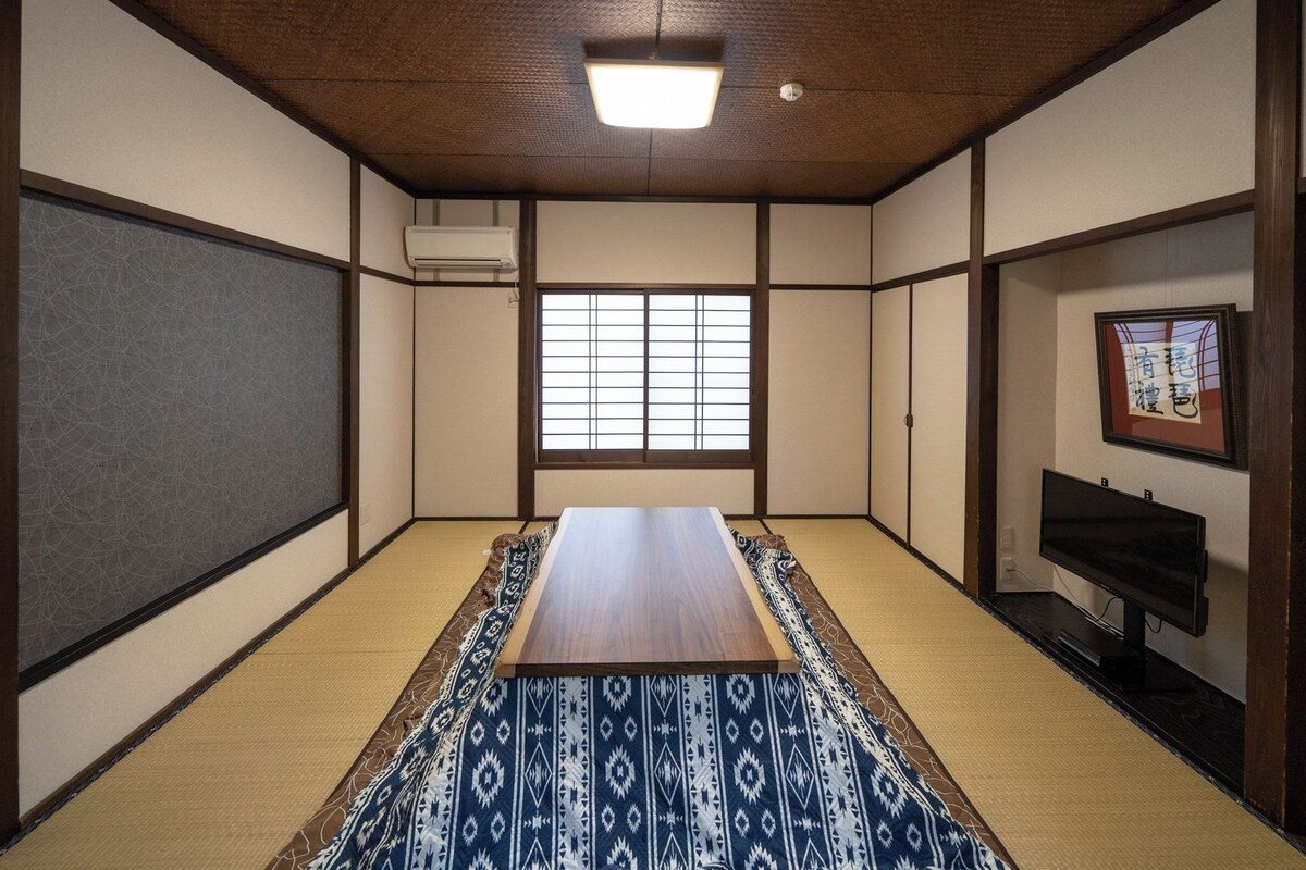 A traditional Japanese room with tatami flooring, a wooden table, a sliding door, and a window with shoji screens.