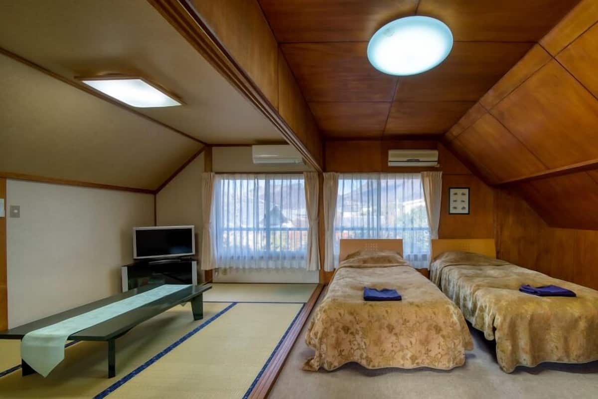 A room with wooden walls, a bed, a bench, a TV, and a window with curtains.