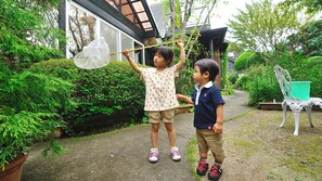 Zwei Kinder spielen mit einem Netz in einem Garten mit einem Haus und einem weißen Stuhl im Hintergrund.