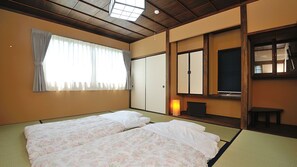 Ein traditioneller japanischer Raum mit Tatami-Bodenbelag, Futon-Bett, Schiebetüren, einem Fernseher und einem kleinen Tisch.