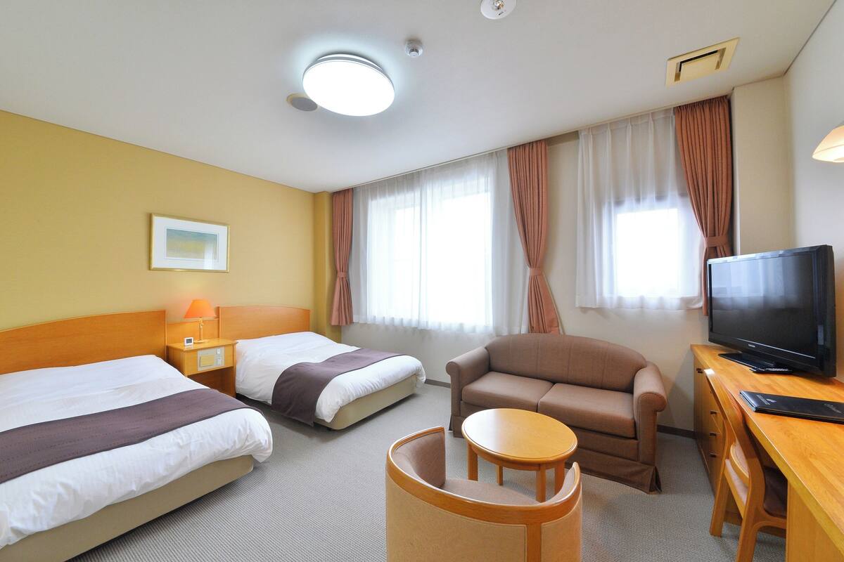 A hotel room with two beds, a sofa, a TV, and a desk.