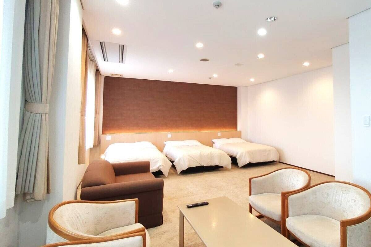 A hotel room with a sofa, armchairs, a small table, and a bed with a headboard.