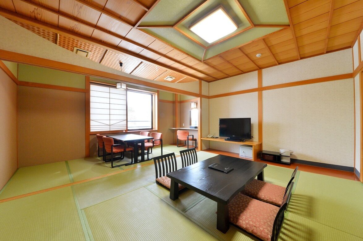 A traditional Japanese room with tatami flooring, a tatami mat table, a television, and sliding doors.
