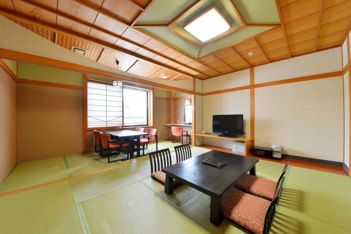A traditional Japanese room with tatami flooring, a tatami mat table, a television, and sliding doors.