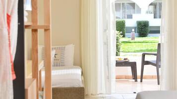 A hotel room with a bed, a small table, and a chair. There is a view of a garden and a building outside the window.