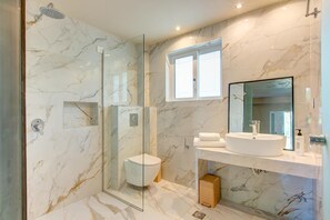 A modern bathroom with a glass-enclosed shower, a toilet, a sink with a mirror, and a window above the sink. - Alykanas Beach Grand Hotel by Zante Plaza (Zakynthos)