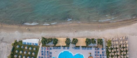 An aerial view of a beachside resort with a swimming pool, sun loungers, umbrellas, and a beach area.