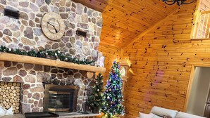 A cozy living room with a stone fireplace, a wooden coffee table, a beige sofa, and a Christmas tree. - Secluded 4-bedroom log cabin surrounded by beautiful forest (New Lisbon)