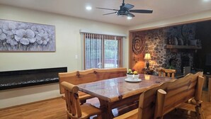 A dining area with a wooden table and benches, a ceiling fan, a stone fireplace, and a window with blinds. - Secluded 4-bedroom log cabin surrounded by beautiful forest (New Lisbon)