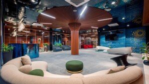 A modern lobby with a central wooden column, seating areas, and a vibrant mural.