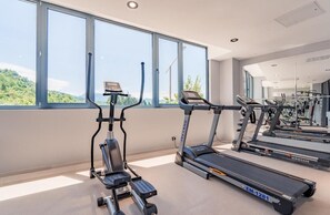 Un gimnasio con cintas de correr, una máquina elíptica y un espejo grande.