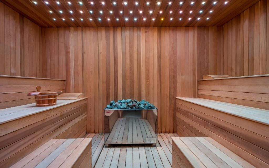 Una sauna con paredes y bancos de madera, un banco central con troncos y un cubo en el banco de la izquierda.