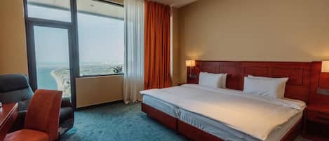 Habitación de hotel con una cama grande, un escritorio, una silla y vistas a la ciudad a través de un ventanal amplio.