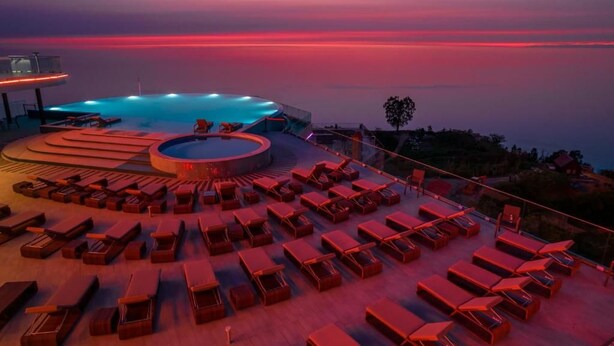 A rooftop pool area with sun loungers and a circular seating area, overlooking a body of water.