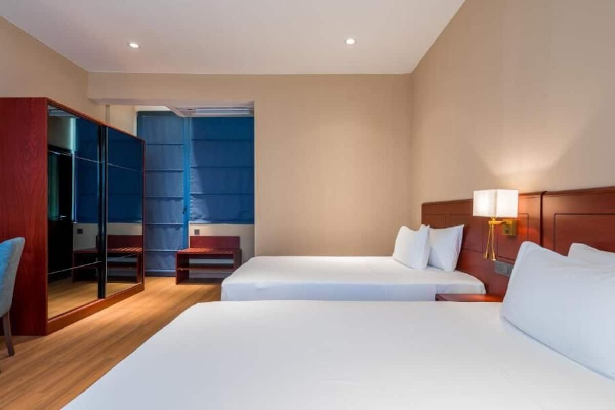 A hotel room with two beds, a desk, a chair, a wardrobe, and a mirror.