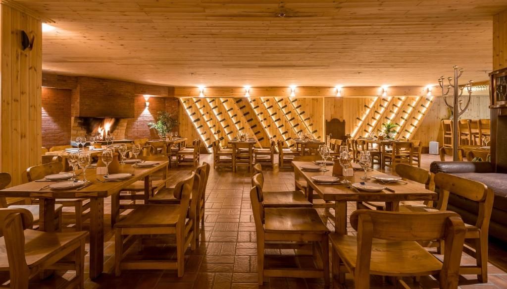 Un restaurante con mesas y sillas de madera, una pared de ladrillo con chimenea, y un techo inclinado con vigas de madera.