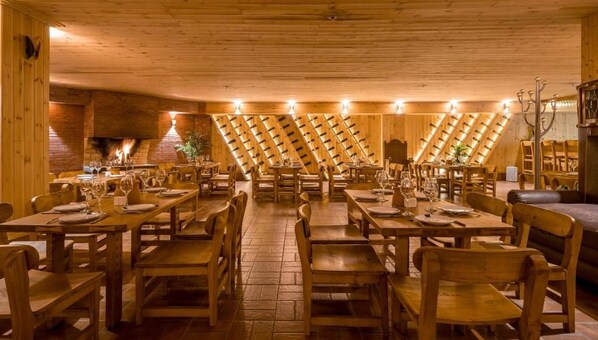 A restaurant with wooden tables and chairs, a brick wall with a fireplace, and a sloped ceiling with wooden beams. - Litz Resort Batumi (Batumi)