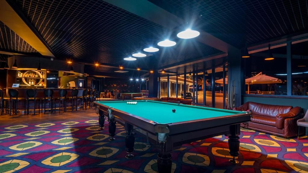 Uma mesa de bilhar em um espaço com carpete estampado, área de bar e sofá de couro.