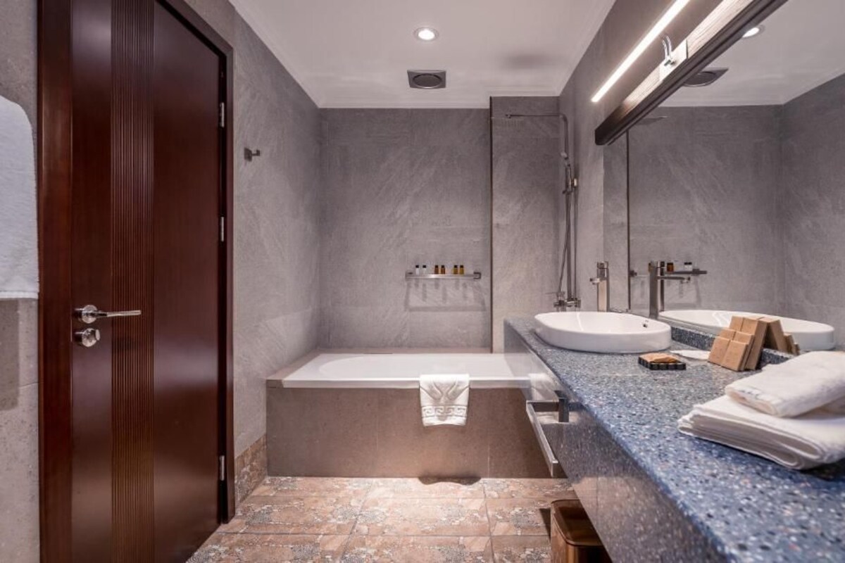A modern bathroom with a wooden door, a bathtub, a sink, and a large mirror.