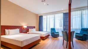 A hotel room with two beds, a sitting area with chairs, and a large window with curtains.