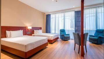 A hotel room with two beds, a sitting area with chairs, and a large window with curtains.