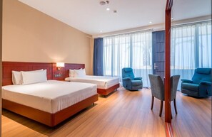 A hotel room with two beds, a sitting area with chairs, and a large window with curtains.