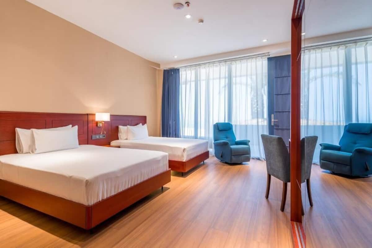 A hotel room with two beds, a sitting area with chairs, and a large window with curtains.