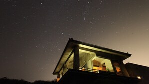 Een modern gebouw met een glazen gevel en een balkon, onder een sterrenhemel.