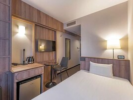 Habitación de hotel con cama, escritorio con hervidor, silla, televisión y lámpara.