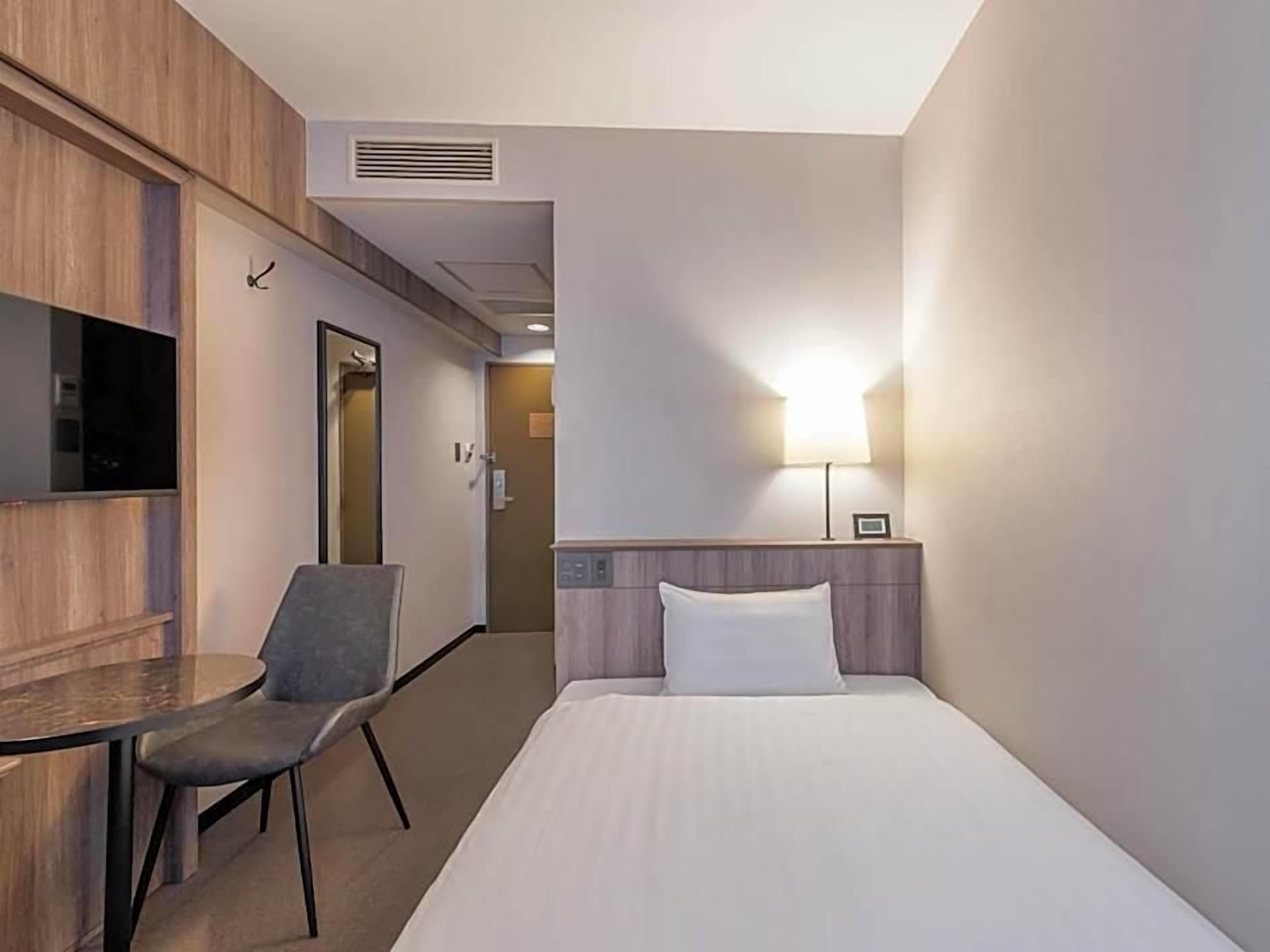 A hotel room with a bed, a desk with a chair, a TV, and a lamp.