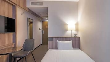 A hotel room with a bed, a desk with a chair, a TV, and a lamp.