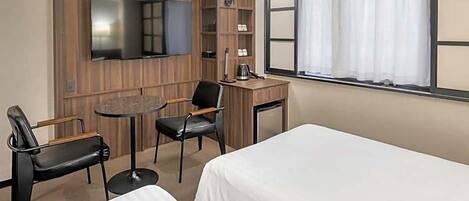 Ein Hotelzimmer mit zwei Betten, einem Schreibtisch, einem Stuhl, einem Fernseher und einem Fenster mit Vorhängen.