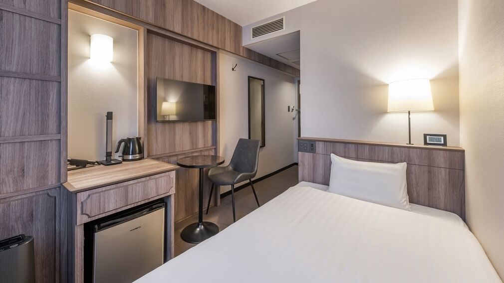 Habitación de hotel con cama, escritorio con silla, televisor, cafetera y refrigerador pequeño.