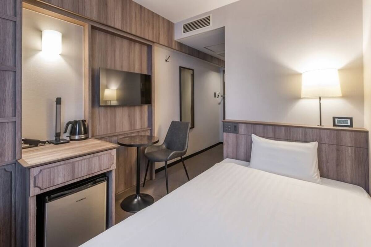 Une chambre d’hôtel comprenant un lit, un bureau avec une chaise, une télévision, une machine à café et un petit réfrigérateur.