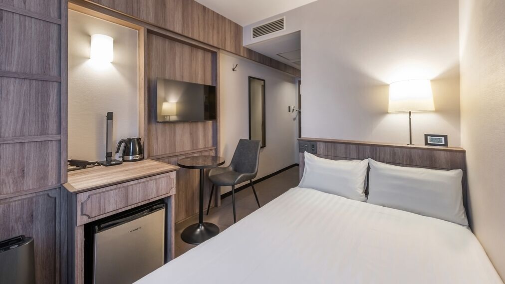 Habitación de hotel con cama, escritorio con cafetera, silla, televisor y refrigerador pequeño.