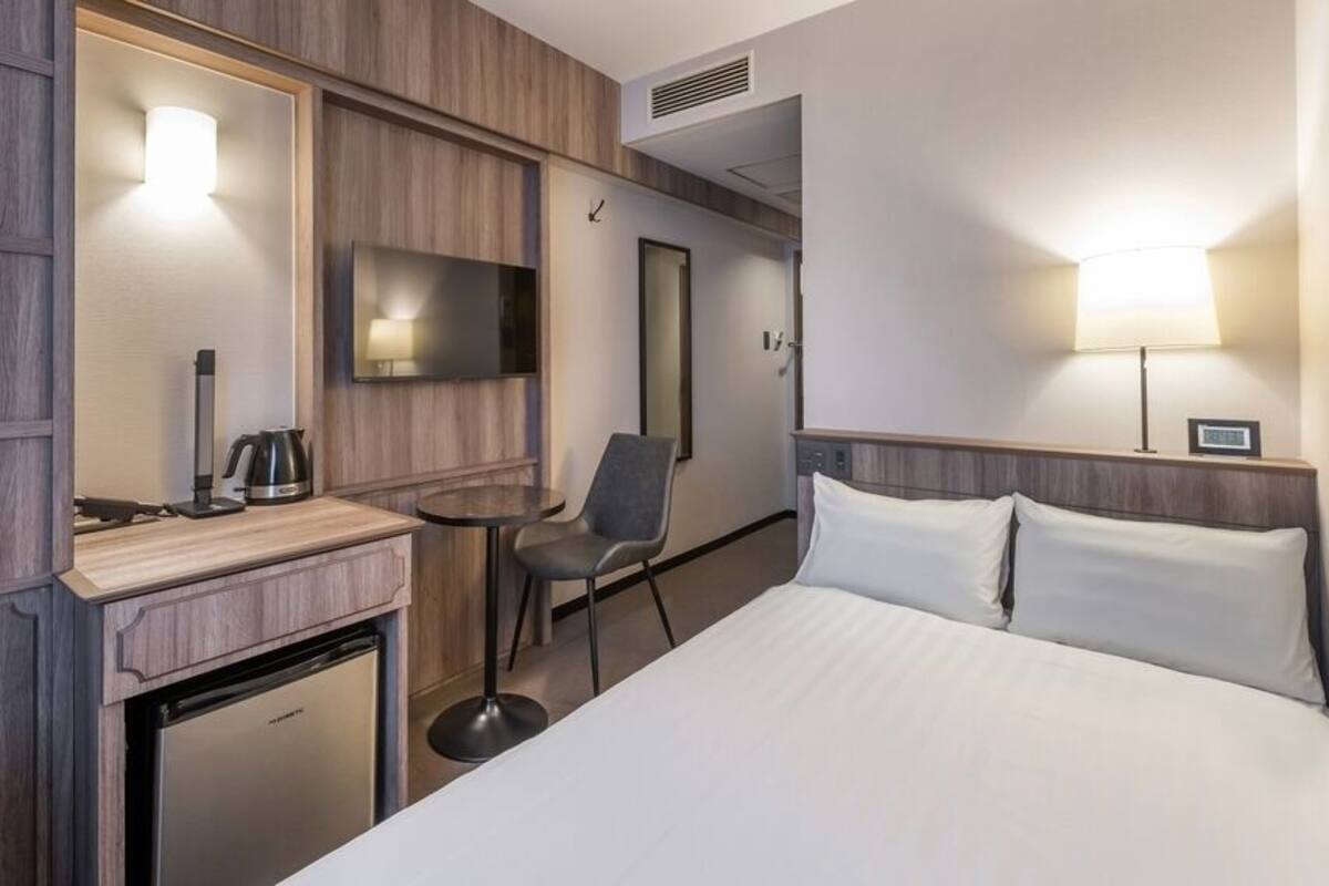 Une chambre d’hôtel équipée d’un lit, d’un bureau avec une machine à café, d’une chaise, d’une télévision et d’un petit réfrigérateur.