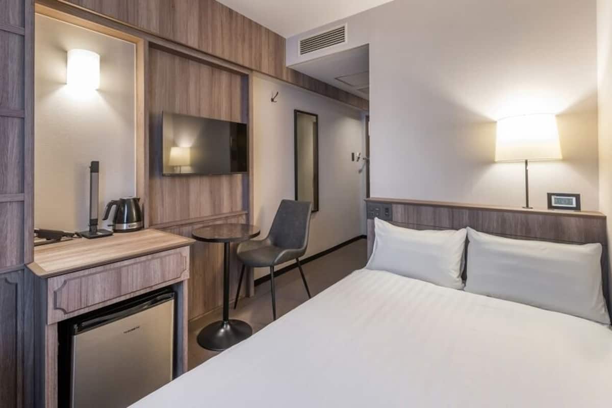 Habitación de hotel con cama, escritorio con cafetera, silla, televisor y refrigerador pequeño.