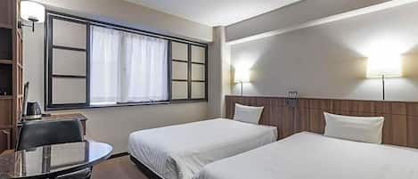 Een hotelkamer met twee enkele bedden, een klein bureau met stoel, een raam met gordijnen en een wandlamp.