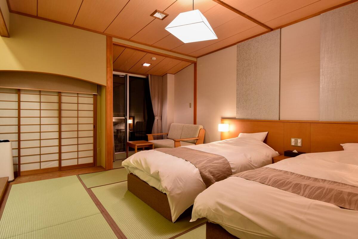 A hotel room with two beds, a sliding door, a chair, and a small table.