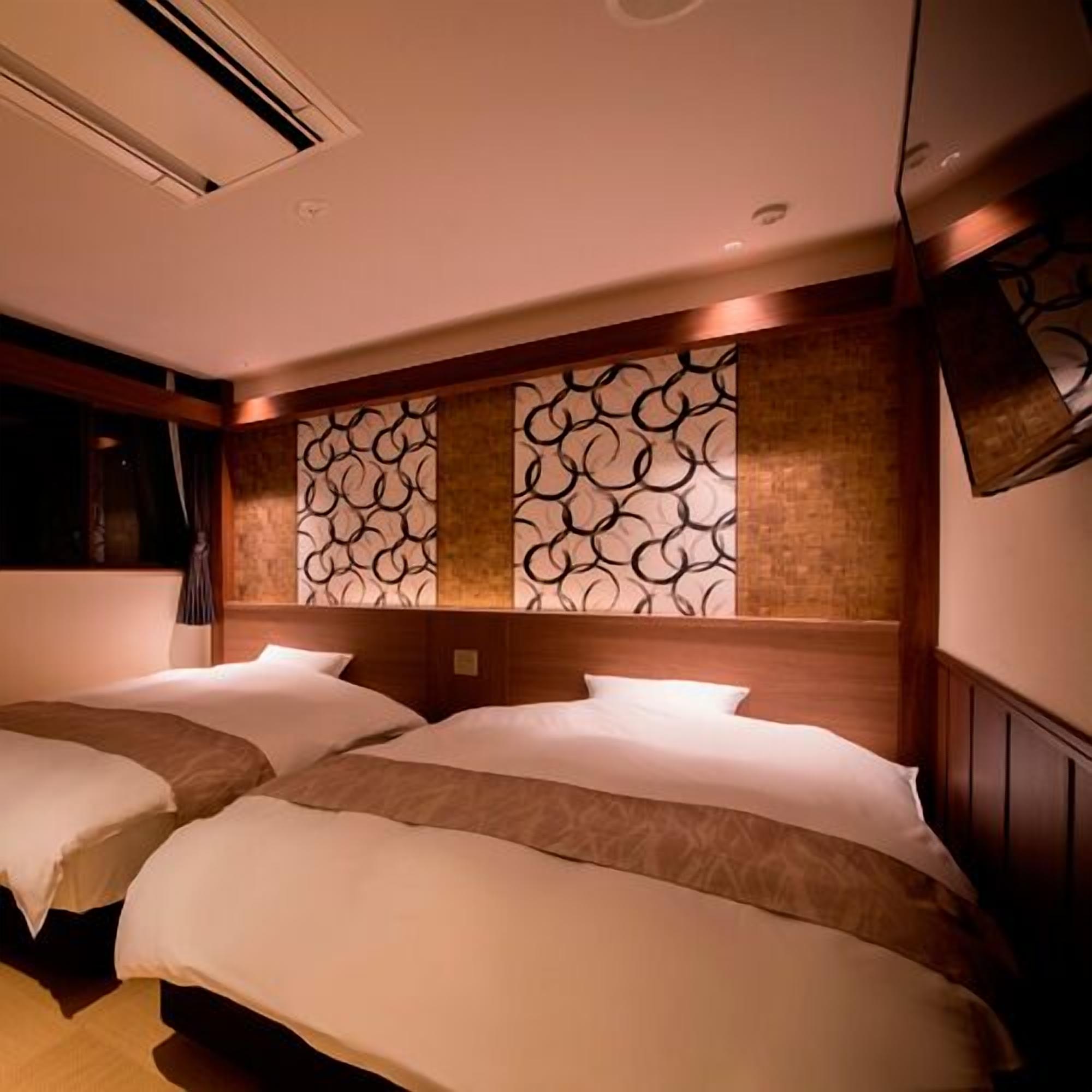 A hotel room with two beds, a wooden headboard, a decorative wall panel, and a mounted television.