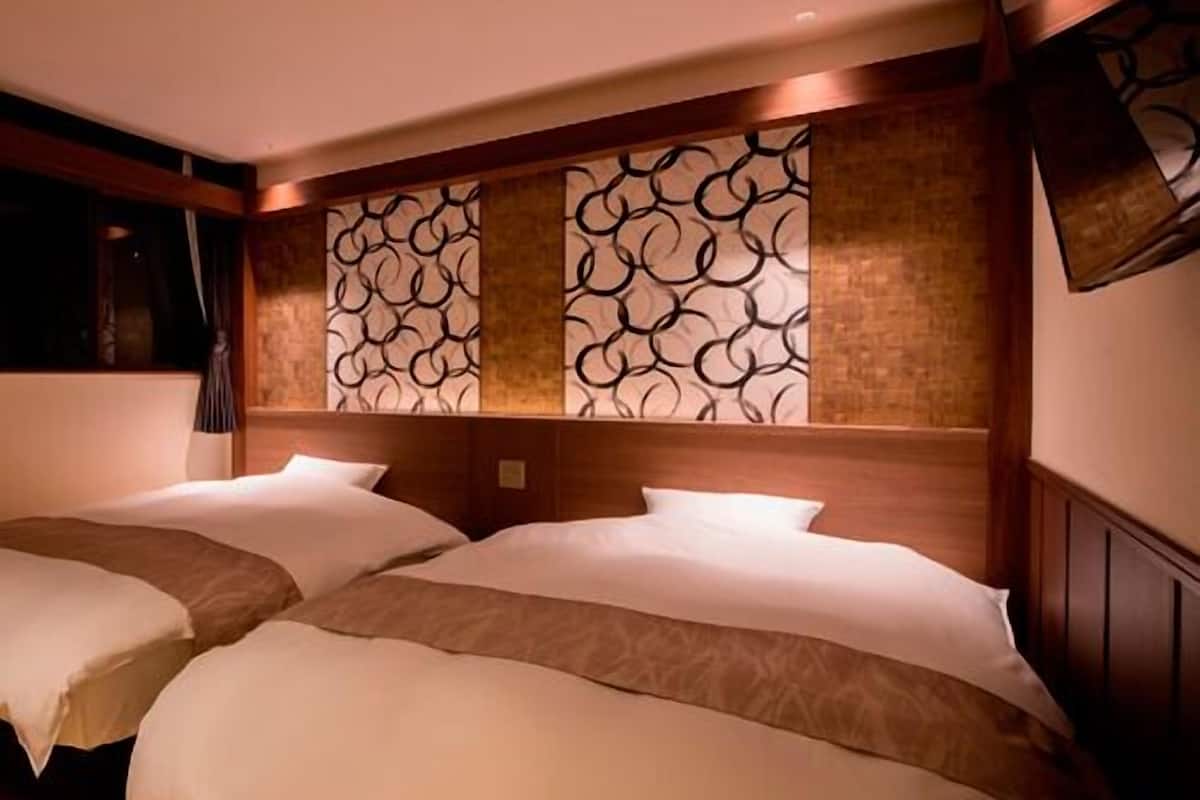 A hotel room with two beds, a wooden headboard, a decorative wall panel, and a mounted television.