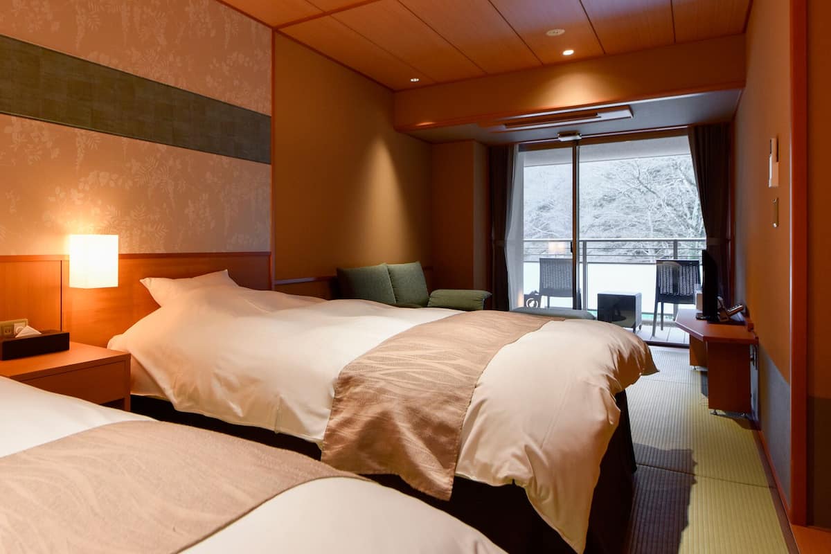 A hotel room with two beds, a large window, and a balcony.