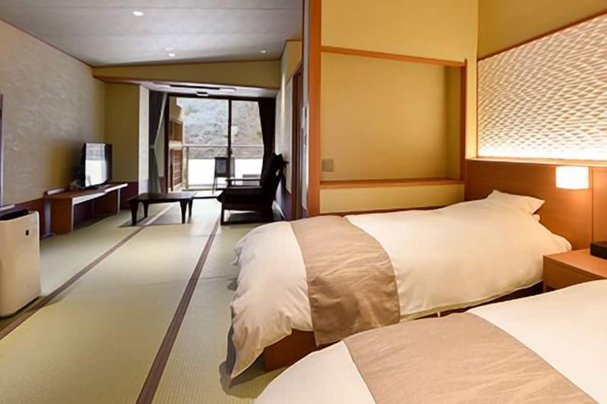 A hotel room with two beds, a desk, a chair, a television, and a view of the outdoors.